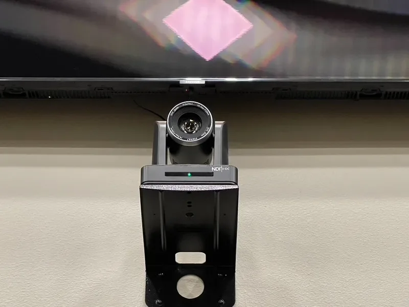 Wall-mounted NDI HX PTZ broadcast camera below the Maple Springs confidence monitor